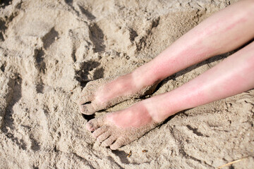 Sunlit sand-covered feet at beach