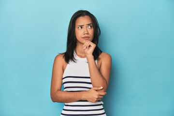 Filipina young woman on blue studio thinking and looking up, being reflective, contemplating,...