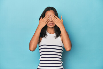 Filipina young woman on blue studio afraid covering eyes with hands.
