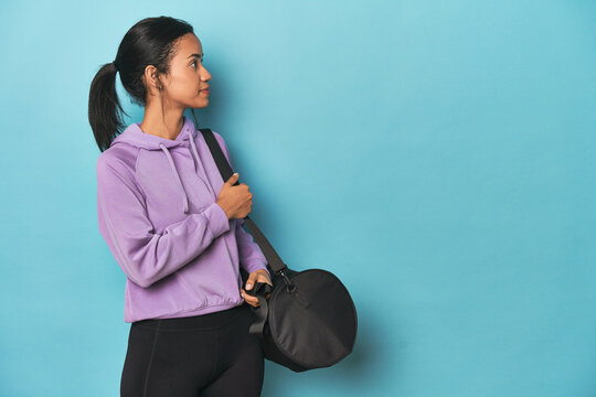 Young Filipina with sports backpack for the gym on blue backdrop