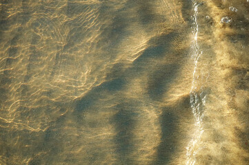 The beach reflects the sunlight on the waves and wet sand. It appears the sand under the water