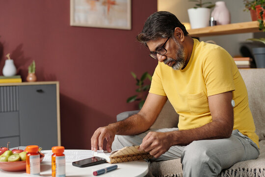 Man reading book indoors with insulin patch and medication nearby