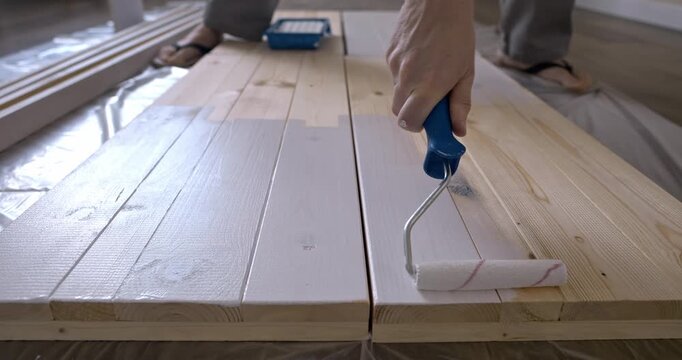 Hand Painting Wooden Planks with White Paint Using Paint Roller DIY Home Improvement and Wood Surface Coating Process on Natural Timber Boards Interior Design. painting of wooden shelving