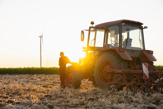 Farmer with tractor and wind turbine in field at sunset promoting sustainability