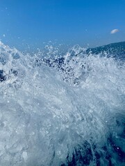 Close up of ocean water splash created by a fast-moving speedboat, captured in daylight under a clear blue sky.
