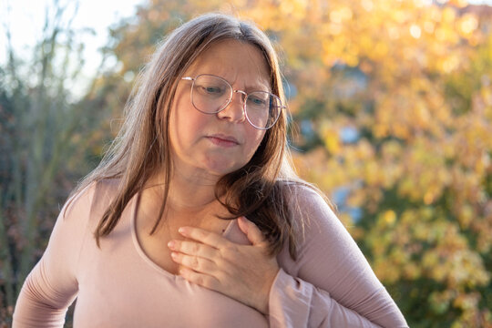 Middle-aged woman experiencing chest pain, pressing hands to heart. Concept of health problems, cardiac arrest, and distress, Health risk, heart failure, and emergency situation