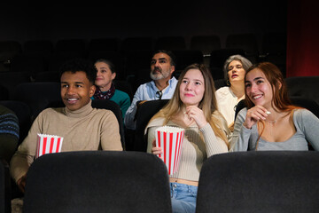 Multi ethnic friends watching a film at the movie theater, having fun together and eating popcorn