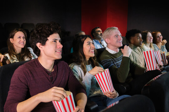 Group of young people watching a movie and eating popcorn at the cinema