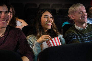 Group of friends watching a movie at the cinema and eating popcorn