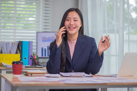Stressed businesswoman in formal attire sits at office desk with laptop, analyzing financial charts and documents under pressure, facing corporate challenges.