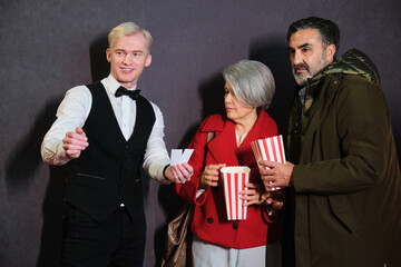 Usher tearing tickets of a couple holding popcorn buckets entering movie theater