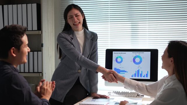 Professional businesswomen networking with businessman, celebrating successful collaboration near computer displaying financial charts and graphs in corporate office setting