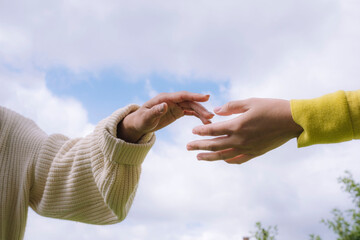 Hands reaching out to connect outdoors beneath a cloudy sky
