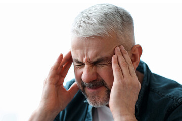 Closeup of mature grey-haired man suffering from headache at home, touching his temples, panorama...