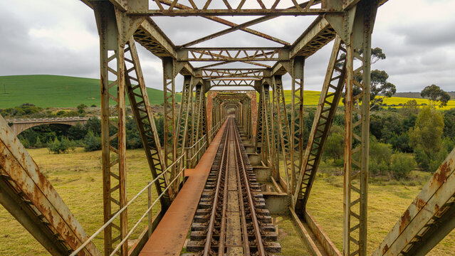 Aerial view of the rusted railway bridge, stretching towards fields of gold under a sky of brooding clouds, Riversdale, Western Cape, South Africa.