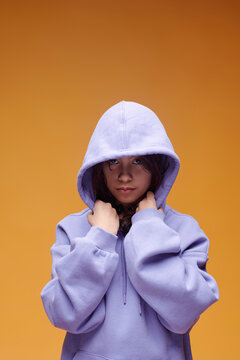 Girl in purple hoodie looking at camera in studio on orange background
