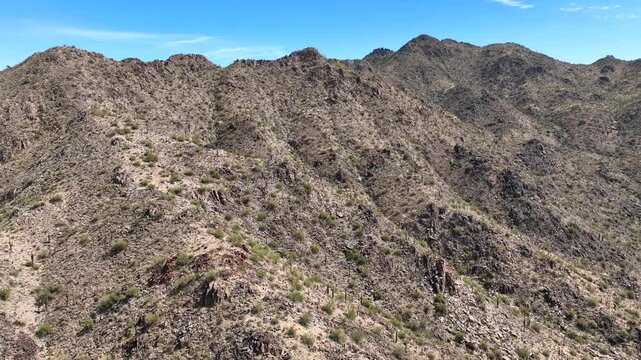 Aerial view of the sun-drenched, rocky terrain of SanTan Mountain, with sparse vegetation under a clear blue sky, SanTan Mountain, Arizona, United States.