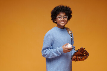 Portrait of smiling schoolboy with baseball glove and ball in studio