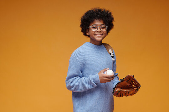 Portrait of smiling schoolboy with baseball glove and ball in studio