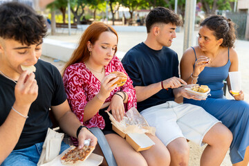 Group of gen z friends enjoying take away food together outdoors