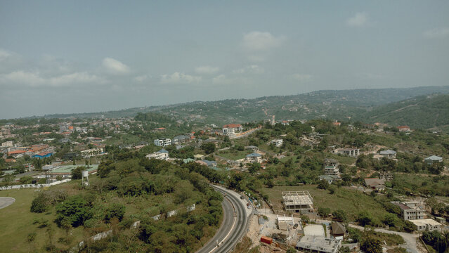 Aerial view of winding roads cutting through lush green hills dotted with buildings, under a vast sky, Aburi, Eastern Region, Ghana.