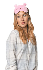 Fototapeta premium Blonde in pajamas with sleep mask looks aside smiling, cheerful and pleasant.