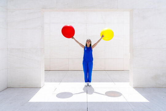 Woman in blue holding red and yellow balloons in minimalist outdoor setting