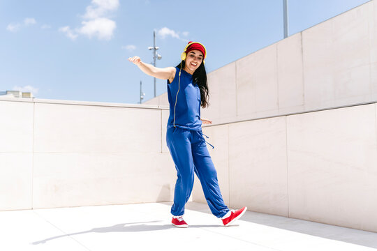 Person dancing outdoors in blue outfit with red shoes and hat