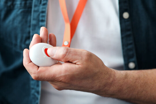 Senior people support concept. Unrecognizable old man pushing red button for emergency while staying home alone, closeup. Male hand holding equipment with panic button, cropped