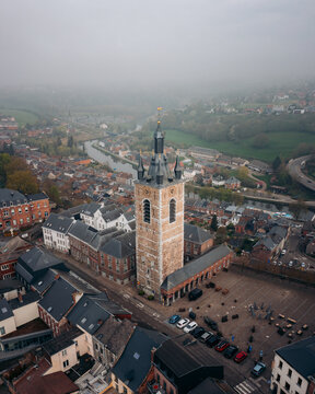 Aerial view of a majestic bell tower rising through a misty cityscape, its stone contrasting with the slate roofs below, Thuin, Wallonia, Belgium.