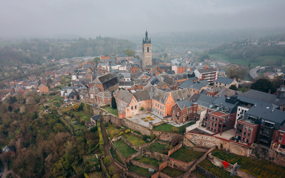 Aerial view of the belfry tower piercing through the misty skyline, amidst terracotta rooftops and terraced gardens, Thuin, Wallonia, Belgium.