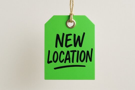 A bright green tag with the text "NEW LOCATION" hangs on a twine, conveying the concept of relocation or change of address in a business context.