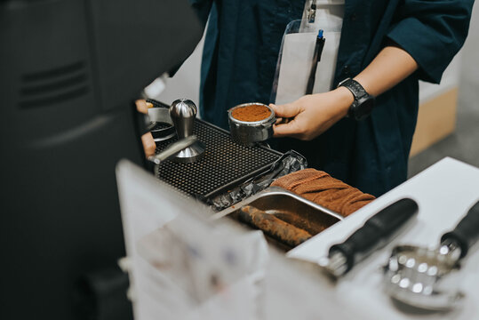 Close-up of hand Barista holding portafilter and coffee tamper making an espresso coffee. - Powered by Adobe