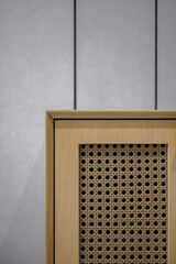 Corner detail of a Japandi style wooden cabinet with a natural rattan cane panel. Minimalist furniture craftsmanship against a modern textured wall.