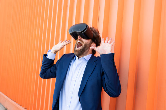 Businessman in suit with VR glasses looking surprised against orange wall