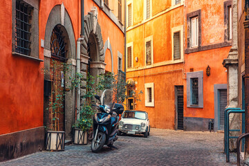 Colorful cobblestone narrow street in Rome city with vintage car, scooter and traditional Italian architecture. Vintage travel, Italian lifestyle and architectural tourism. Travel destination