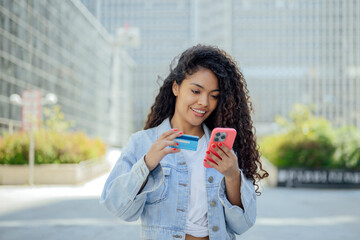 Woman holding credit card and smartphone outdoors in city