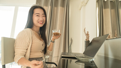 beautiful woman holding coffee mug on hand while using laptop computer at home