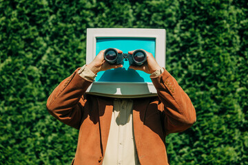 Person with retro monitor head using binoculars outdoors visual metaphor