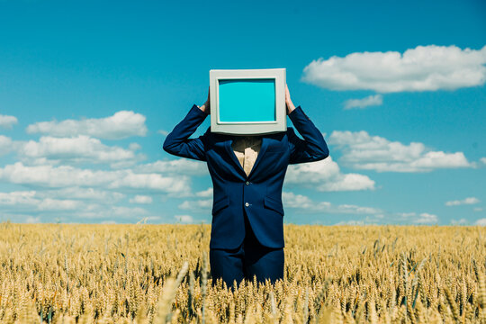 Businesswoman with retro monitor as head in wheat field under blue sky