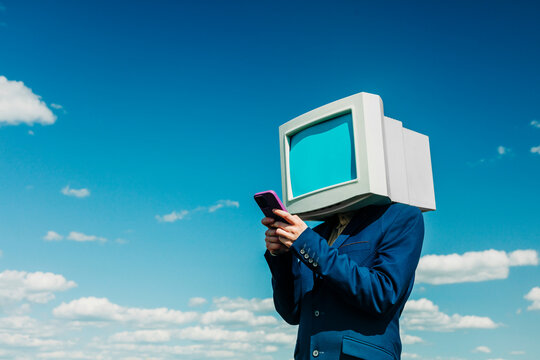 Businesswoman with retro monitor head using smartphone outdoors under blue sky