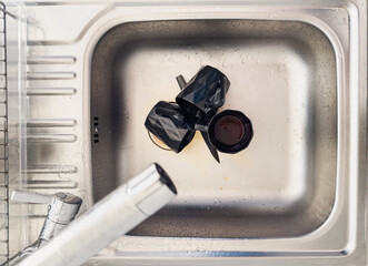 Dirty black mugs in stainless steel kitchen sink, showing everyday home cleaning tasks, mess and...