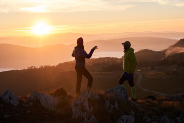 A joyful couple celebrates their victorious ascent to the mountain summit, embracing each other...