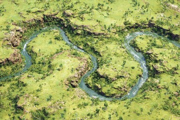 Aerial view of a winding river flowing through a green landscape with rocky terrain