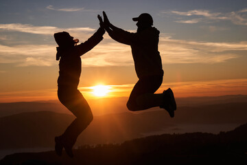 A joyful couple celebrates their victorious ascent to the mountain summit, embracing each other with smiles and excitement, surrounded by breathtaking natural scenery.
