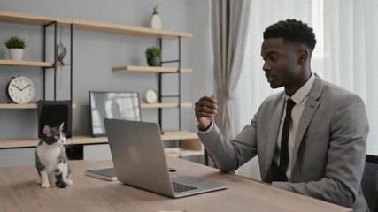 Young professional engaging in a virtual meeting while his cat observes from the desk, blending work and home life seamlessly. - Powered by Adobe