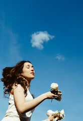 Young woman dancing with white roses under a clear blue sky