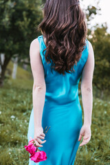 Back view of young woman walking in garden holding pink roses