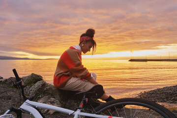 Outdoor portrait of happy african woman admiring sunset over the lake during bike ride