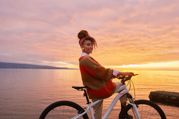 Outdoor portrait of happy african woman admiring sunset over the lake during bike ride